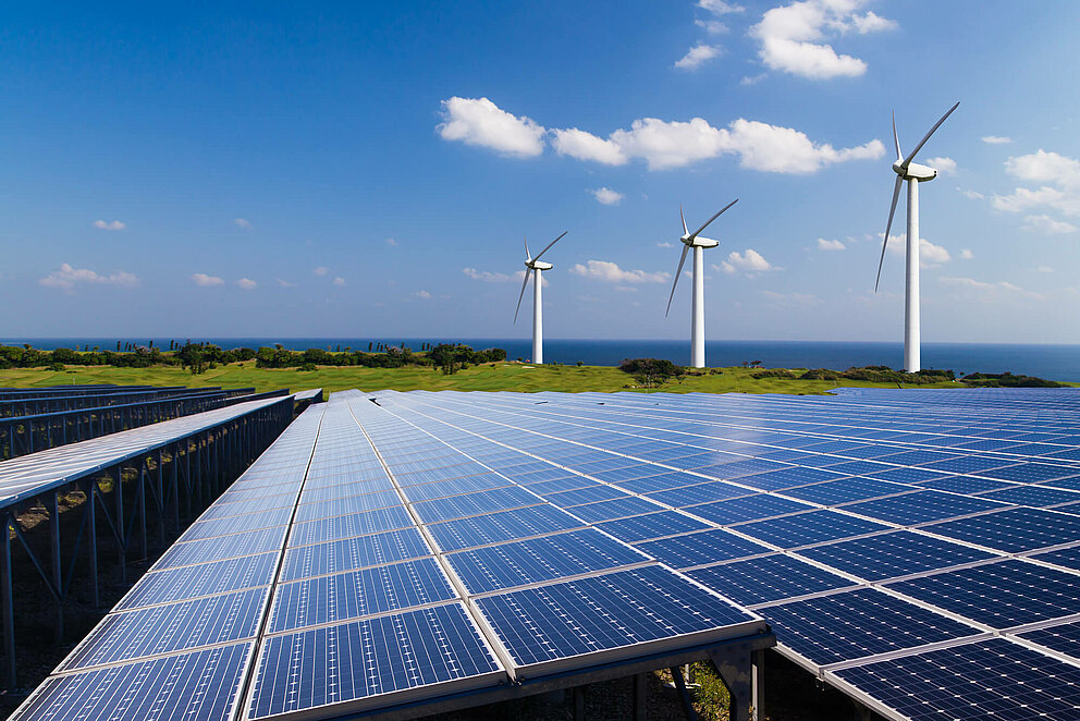 Ein Solarpark mit Windrädern im Hintergrund.