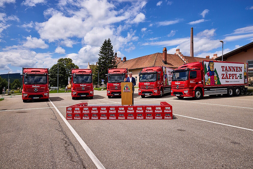 5 elektrische Lkw stehen hinter einer Bühne. Lkws und Bühne ist in Rothaus-Rot gebrandet.