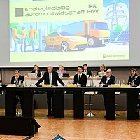 Ministerpräsident Winfried Kretschmann eröffnet das Top-Level-Meeting auf dem Strategiedialog Automobilwirtschaft BW. Er ist umgeben von anderen wichtigen Vertreter:innen der Industrie.