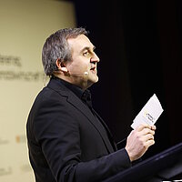 Portrait von Dr. Wolfgang Fischer, Prokurist der Landesagentur e-mobil BW, mit Mikrofon und Moderationskarten.
