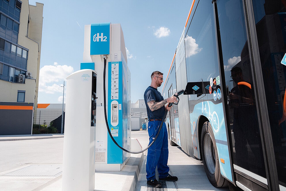 Ein Brennstoffzellenbus wird an einer Wasserstofftankstelle von einem Mann betankt.