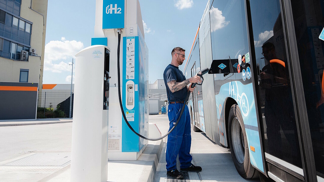 Ein Brennstoffzellenbus wird an einer Wasserstofftankstelle von einem Mann betankt.