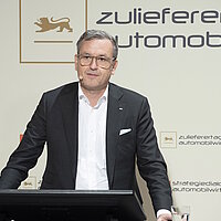 Dr. Jochen Weyrauch steht auf einer Bühne, vor ihm ist ein Monitor und im Hintergrund eine Wand mit der Aufschrift "Strategiedialog Automobilwirtschaft BW"