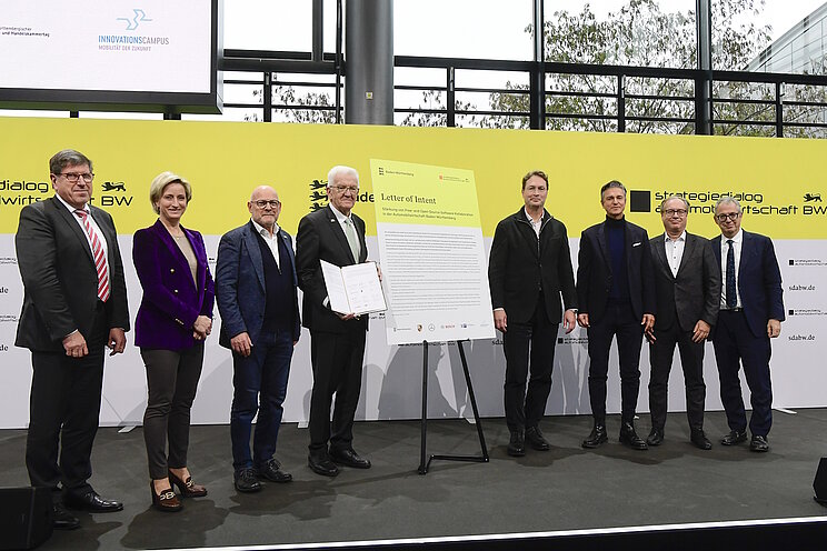 Eine Ansammlung von Personen auf dem Podium des Strategiedialogs Automobilwirtschaft BW. Ministerpräsident Winfried Kretschmann hält ein wichtiges Dokument in der Hand.